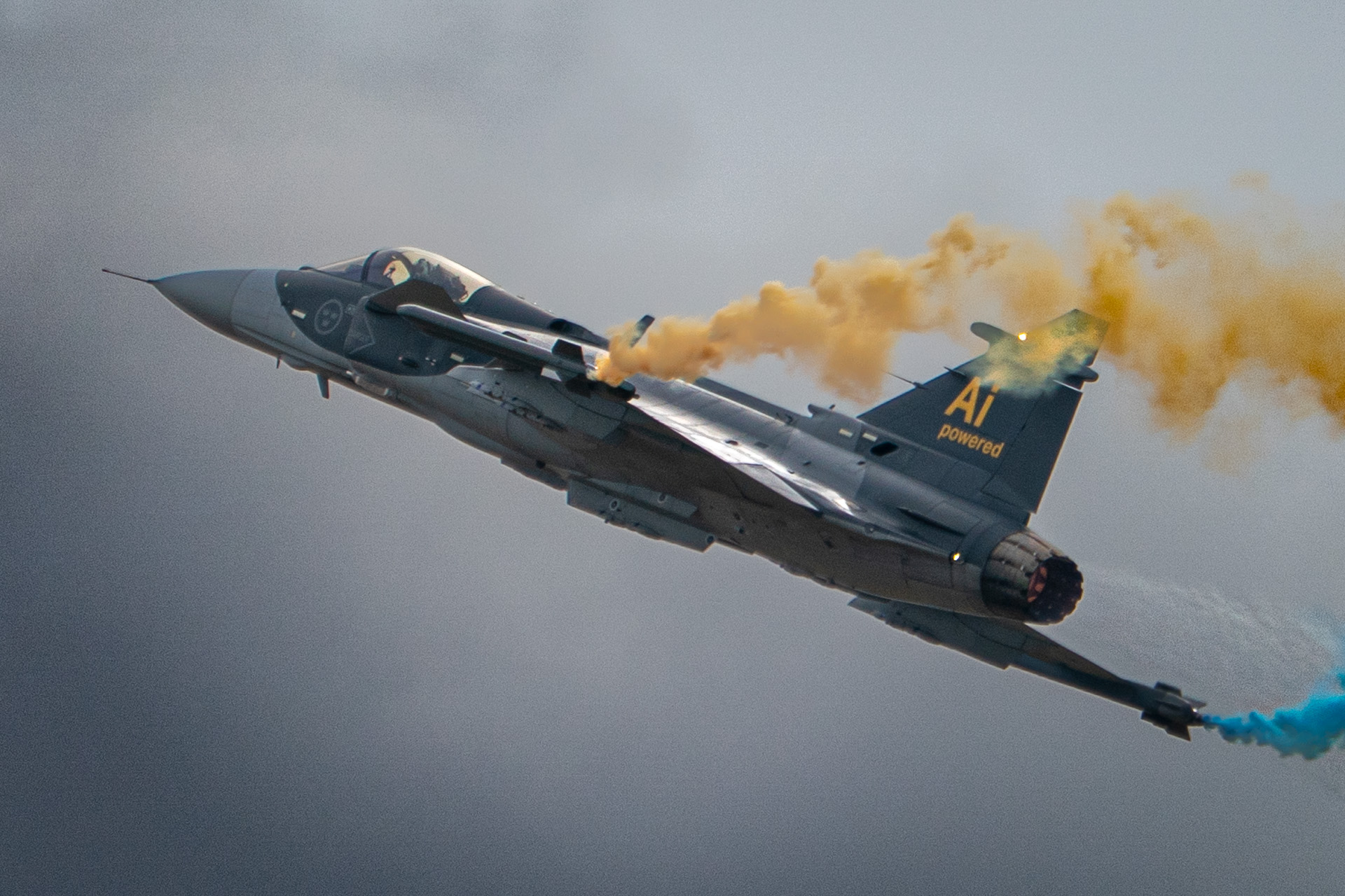 Swedish Air Force Gripen trailing blue and yellow smoke during a centennial flight display